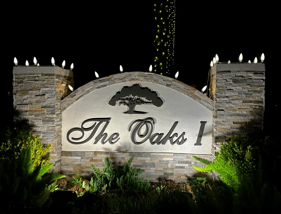 The Oaks stone entrance monument with warm accent lighting at night