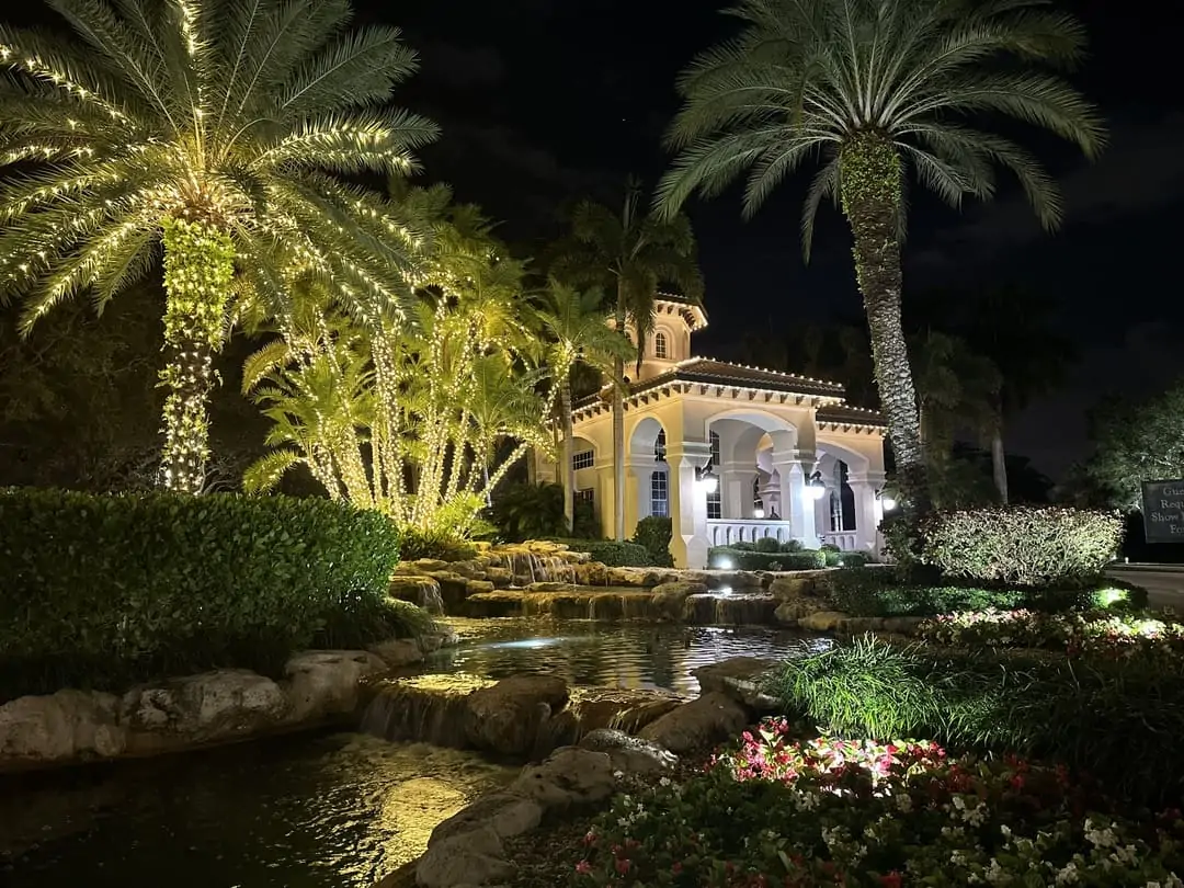 Community clubhouse beside a pond with palms in warm white lighting