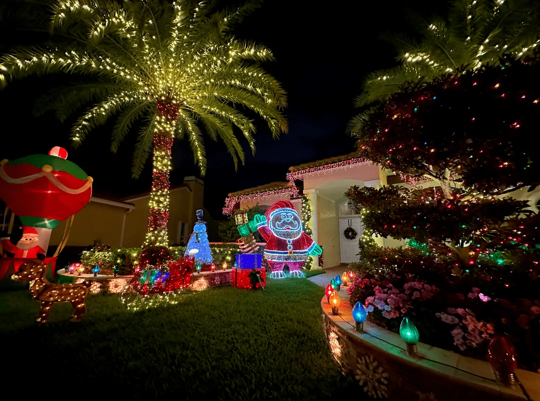Festive home lawn with holiday inflatables and a lit palm tree