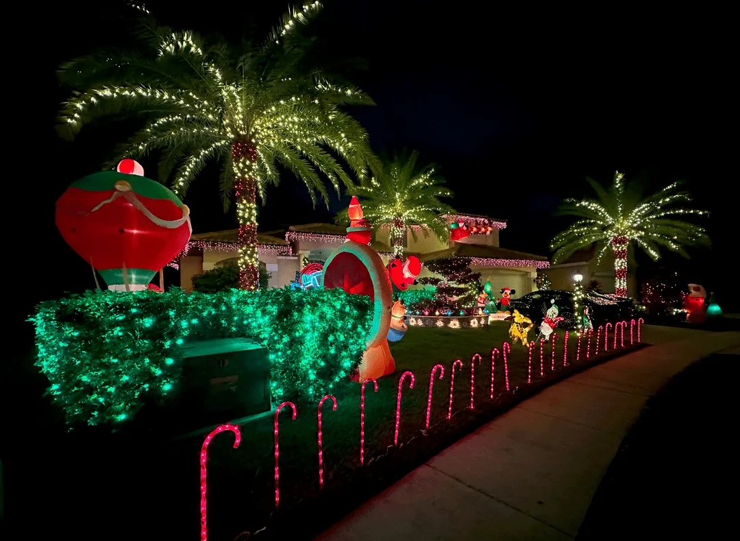Holiday yard with inflatables, a candy-cane lit path, and lit palms