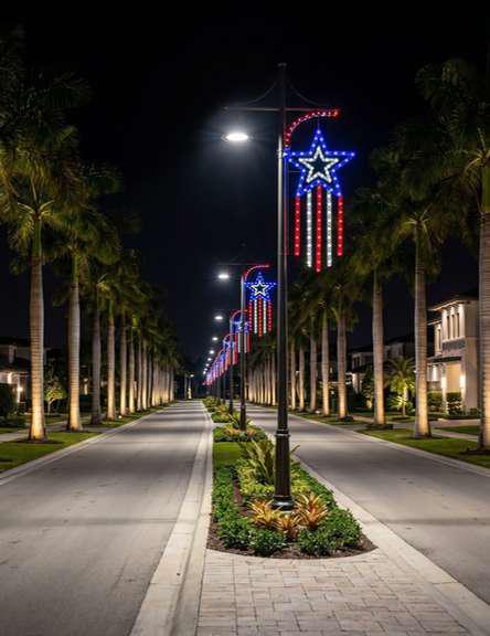 Community boulevard lined with illuminated red, white, and blue star and stars-and-stripes displays on lampposts